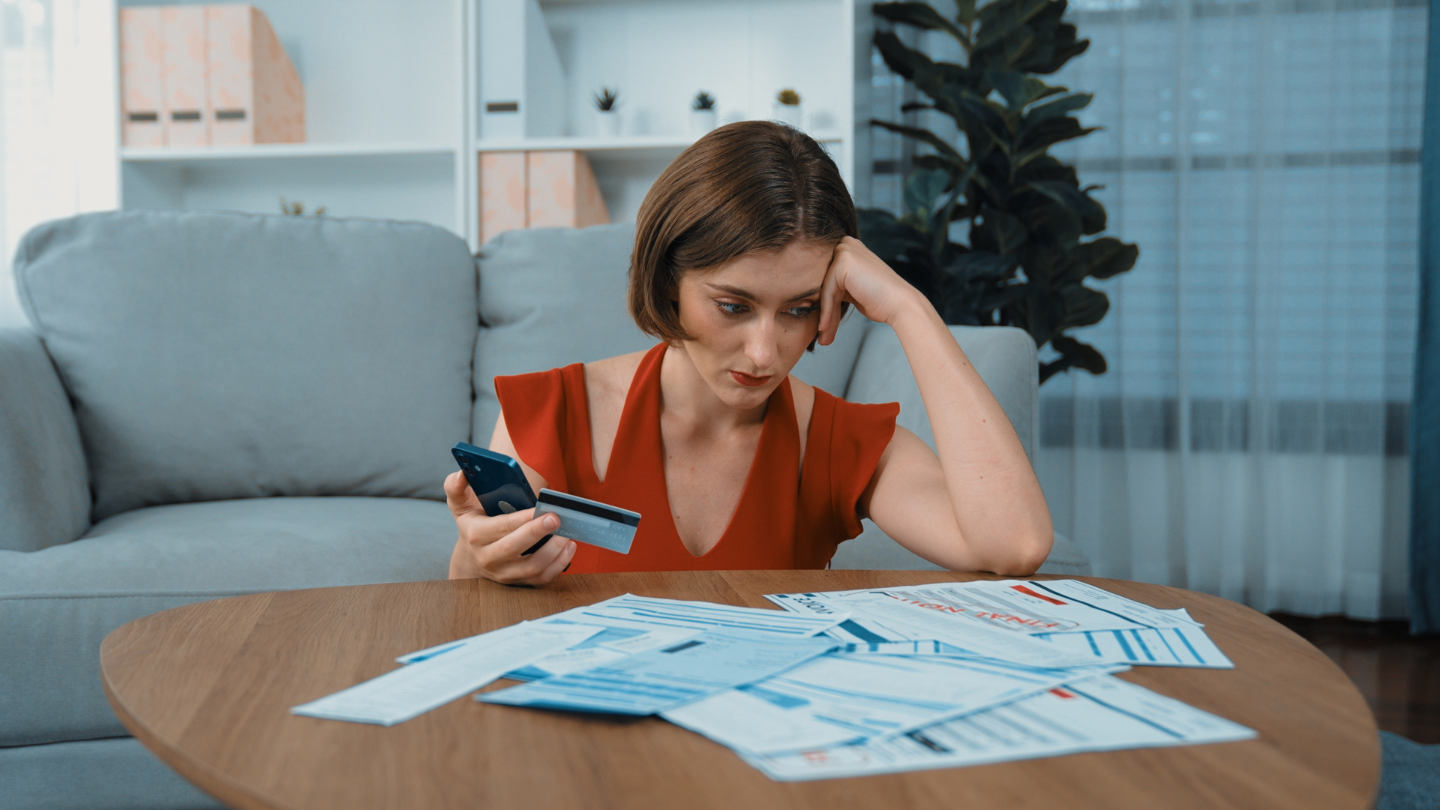 Mujer estresada mirando sus cuentas, con sus tarjetas de crédito en la mano