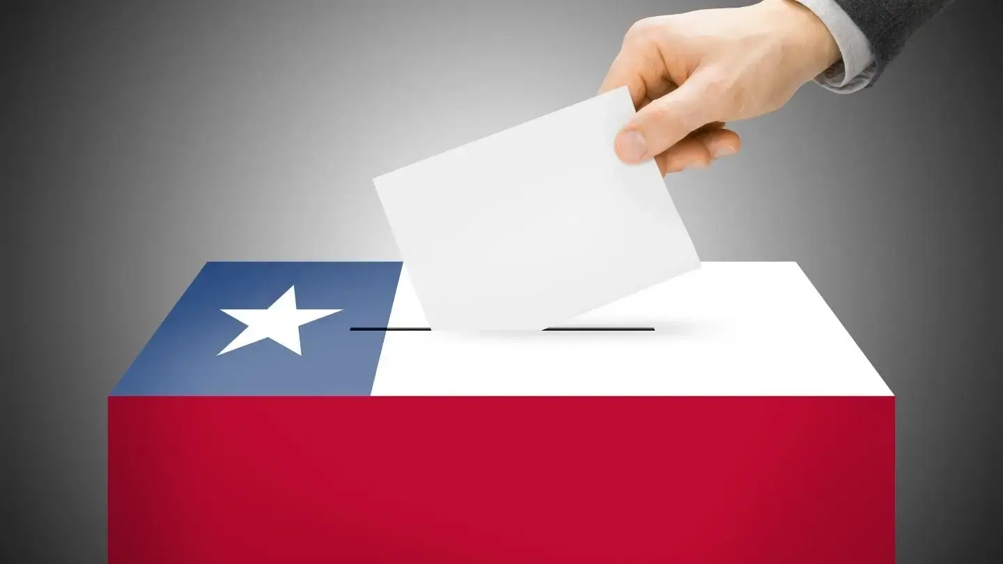 Multa por no votar en elecciones presidenciales Chile. Mano depositando papeleta en urna con bandera de Chile