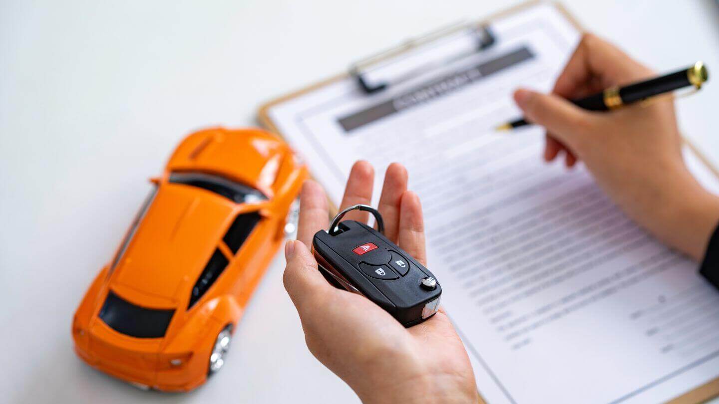 Qué pasa si no pago mi crédito automotriz. Mujer firma documento sosteniendo llaves de auto.