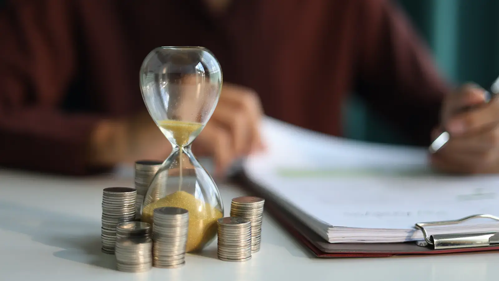 Gastos hormiga. Reloj de arena corriendo al lado de una monedas