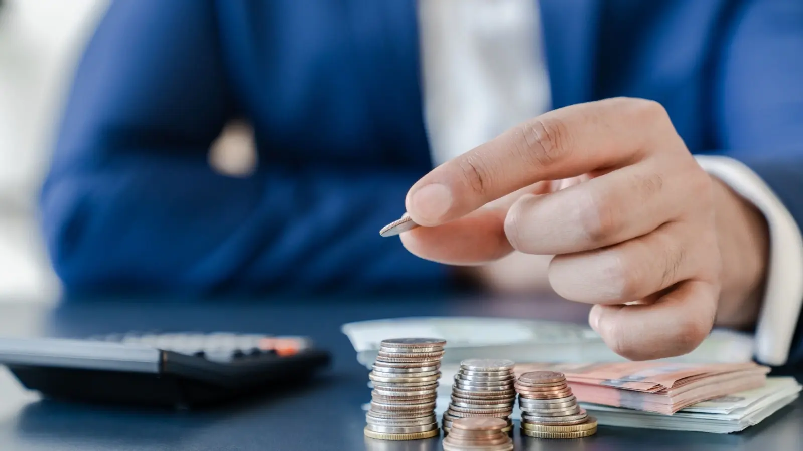 Hombre sujetando una moneda sobre tres pilas de monedas más